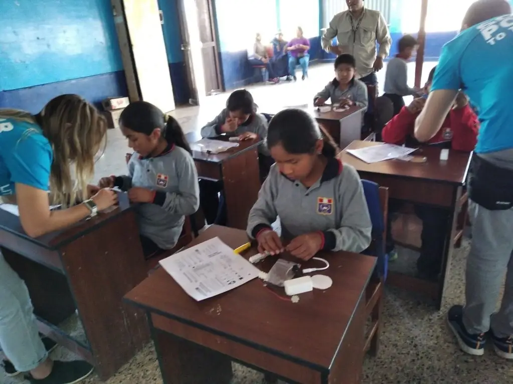 Crianças sentadas em carteiras escolares participando da oficina