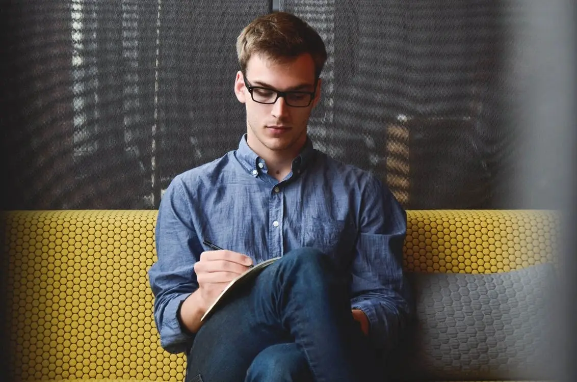 A man with glasses sitting and writing.