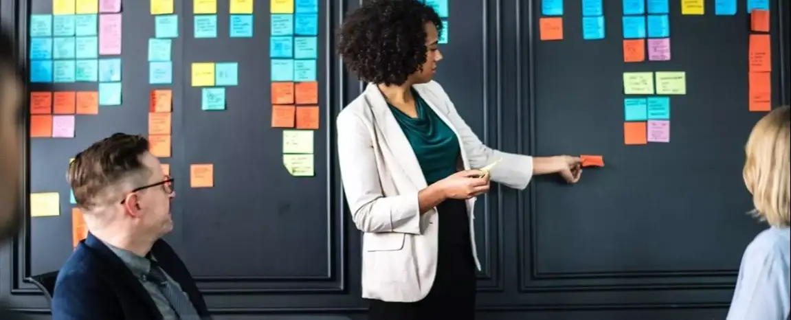 Young professional at a black board putting up sticky notes during a meeting.