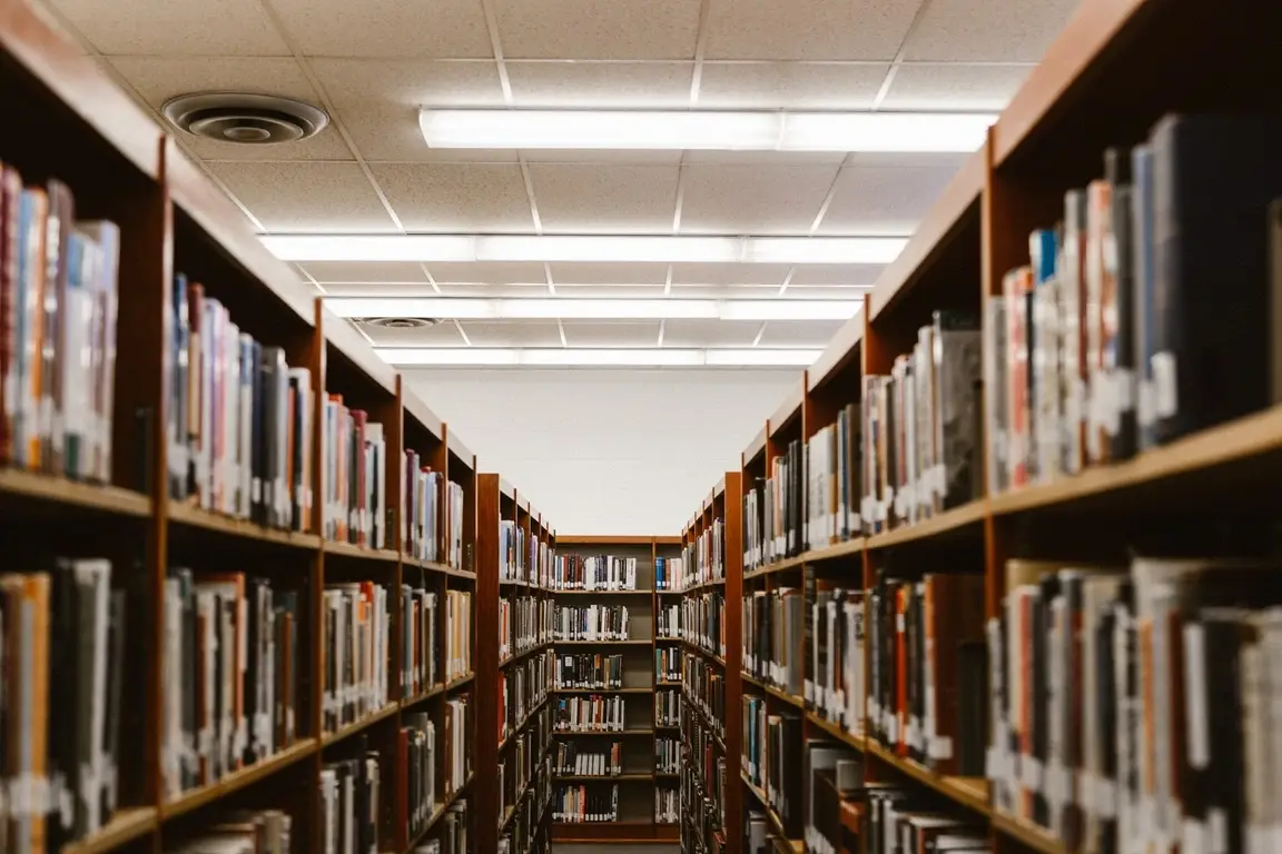 An aisle in a library showing full bookshelves on either side and at the end