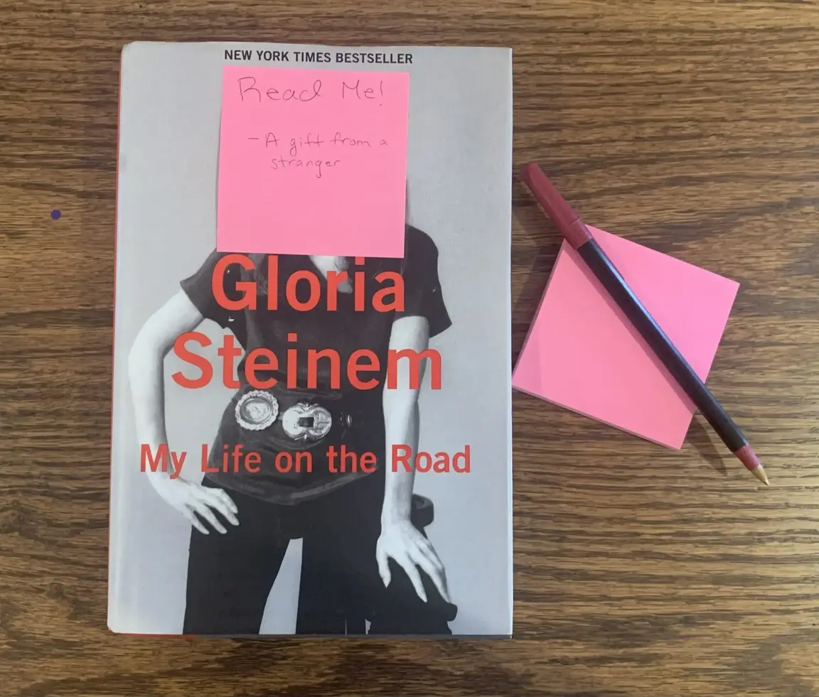 A sticky note affixed to the cover of the Gloria Steinem book.