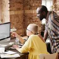 White woman with cancer sits at desk next to Black co-worker.