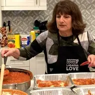 person wearing apron preparing trays of lasagna