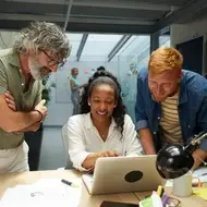 Multiracial colleagues gather around a laptop on a desk planning at a nonprofit.