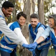 Imagem de 5 voluntários com coletes azuis unidos com as mãos juntas.