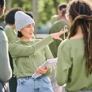 Young woman has a career as a community organizer, wearing long-sleeve green shirt as she stands outside with volunteers dressed similarly.