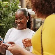 Two Black women talk outside, exchanging contact information as they network at a career event.