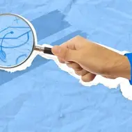 A hand holding a magnifying glass hovers over a drawing of a graduation cap.