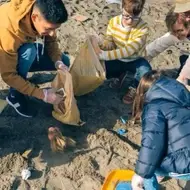 Imagem de crianças recolhendo objetos na areia de uma praia.