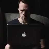 Um homem sentado em um sofá olhando para seu laptop.