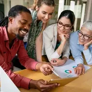 A group of co-workers smile while reviewing an infographic in a meeting room, fostering collaboration.