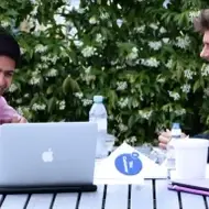 Imagem de 4 jovens reunidos ao redor de uma mesa de madeira, com um notebook, cadernos e garrafas de água.