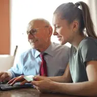 Una mujer enseña a un adulto mayor a utilizar la computadora.