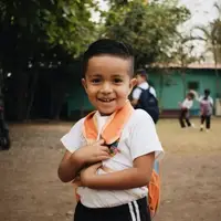 San Jeronimo student with his backpack on smiling at the camera while two students dance in the background