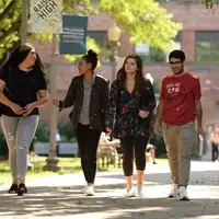 three female student and a male student walk through a courtyard on a pleasant fall afternoon