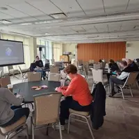 Attendees sit at round tables in a bright, windowed room with a presentation screen displaying "SONIC CONNECTIONS."