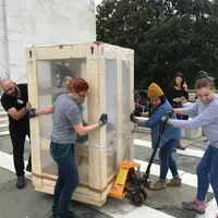 5 Folger staff working together to bring out exhibits; hauling a large exhibit object outside in front of Folger steps prepping for renovation