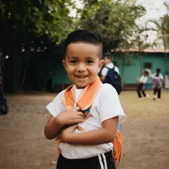 San Jeronimo student with his backpack on smiling at the camera while two students dance in the background