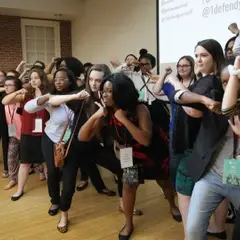 A very horizontal photo of a group of Defend Yourself students, all college aged women, most of them showing how they would do an elbow strike.