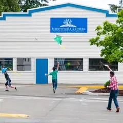 Three middle school boys fly kites in front of the school.