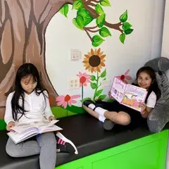 Two young girls reading books on a new bench under a mural of a tree and flowers.