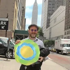 A man holding the Idealist logo poses in the street.