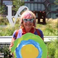 A woman with pink hair holds up the Idealist logo.