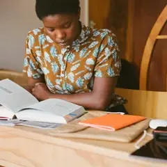 A Black person looks down at a page in their textbook.