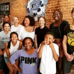 10 women and nonbinary adults of diverse races smiling at the camera. The child of one of them (about 6 years old) joins them.