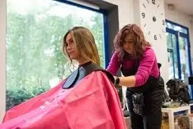 Mujer preparándose para cortarle el pelo a otra mujer.