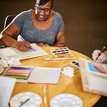 Woman sitting at a table with art supplies around her, working on an art project.