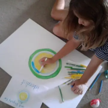 A little girl drawing the Idealist logo.