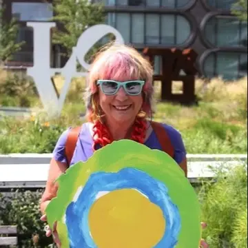 A woman with pink hair holds up the Idealist logo.