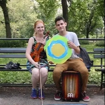 Two people sit next to each other in the park holding the Idealist logo.