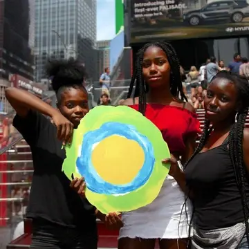 Three children hold up the Idealist logo on the stairs in Times Square.