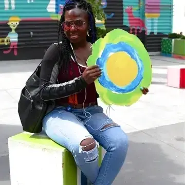 A imagem mostra uma pessoa sentada em um bloco verde, usando fones de ouvido e segurando um cartaz com o símbolo Idealist.