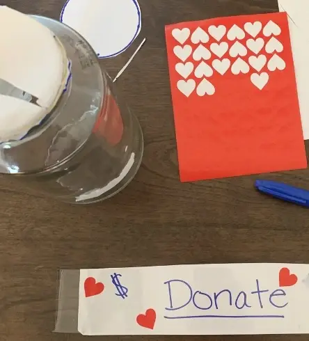 Craft supplies including heart-shaped stickers, a blue sharpie, and a piece of paper that says "Donate."