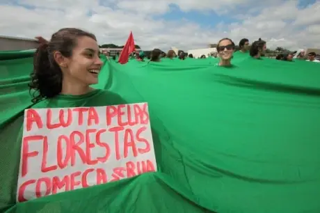 A luta pelas florestas começa na rua - poster segurado por uma mulher vestindo junto com outras pessoas um pano verde contínuo, como se fosse uma floresta