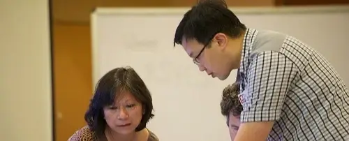 Three people working together. Two of them are sitting and one is standing and leaning over the table.