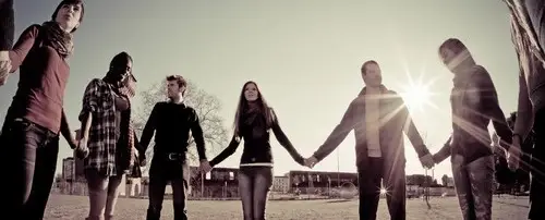 A group of people stand in a half circle with their hands clasped.