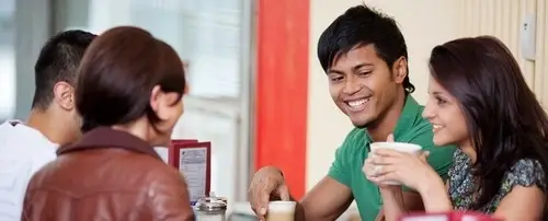 A group of people sitting and talking. Two of them are drinking coffee.