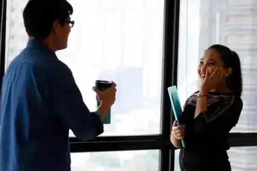 Dois colegas de trabalho conversando perto da janela.