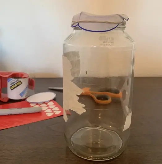 A small paper circle attached to the top of a clean jar with a rubberband, with stickers and scissors in the background.