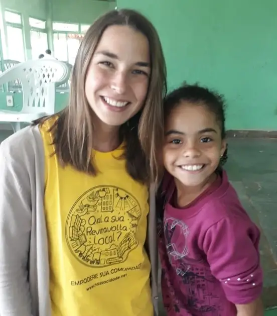 Uma pessoa adulta e uma criança em pé lado a lado, vestindo camisetas coloridas, em um ambiente interno com paredes verdes.