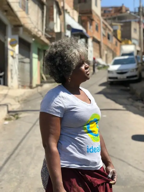 Tia Lu, vestindo uma camiseta com o símbolo idealista no meio de uma rua sem movimento.