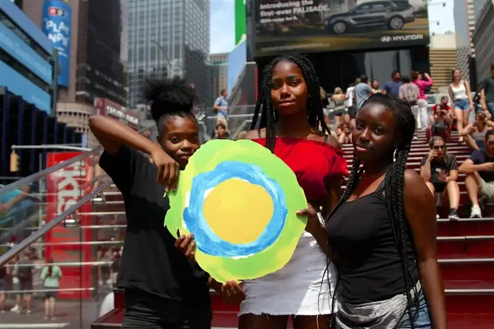 Three teenagers hold the Idealist logo between them.