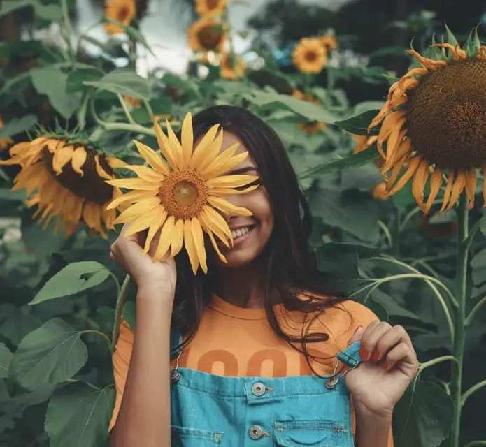 A woman hides half her smile behind a sunflower.