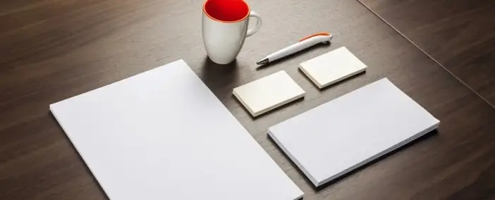 Different sizes of paper and a coffee and pen on a desk.
