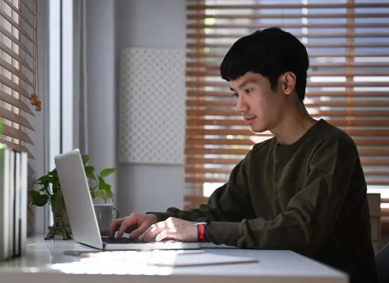 Joven trabaja con una computadora desde casa.