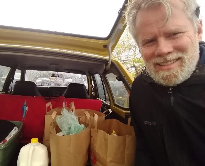 Homem com compras e mantimentos no porta-malas do carro